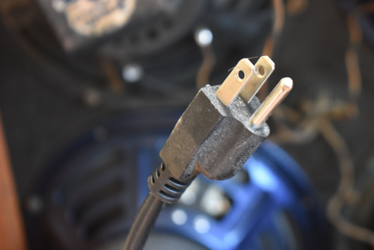 Close-up of the amplifier's black, two-prong power plug, showing dust on the plastic and some wear on the brass prongs.