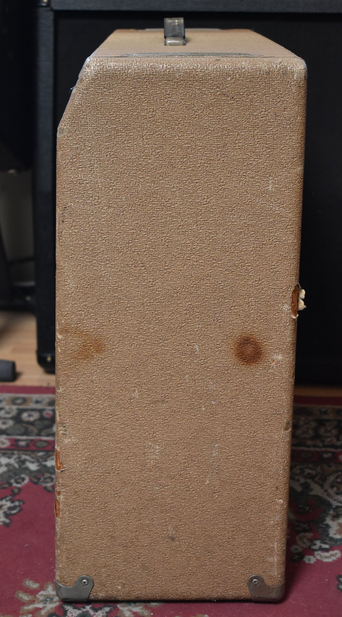The brown textured amplifier is viewed from the right side, showing a top handle, two dark stains, and worn corners with metal caps.