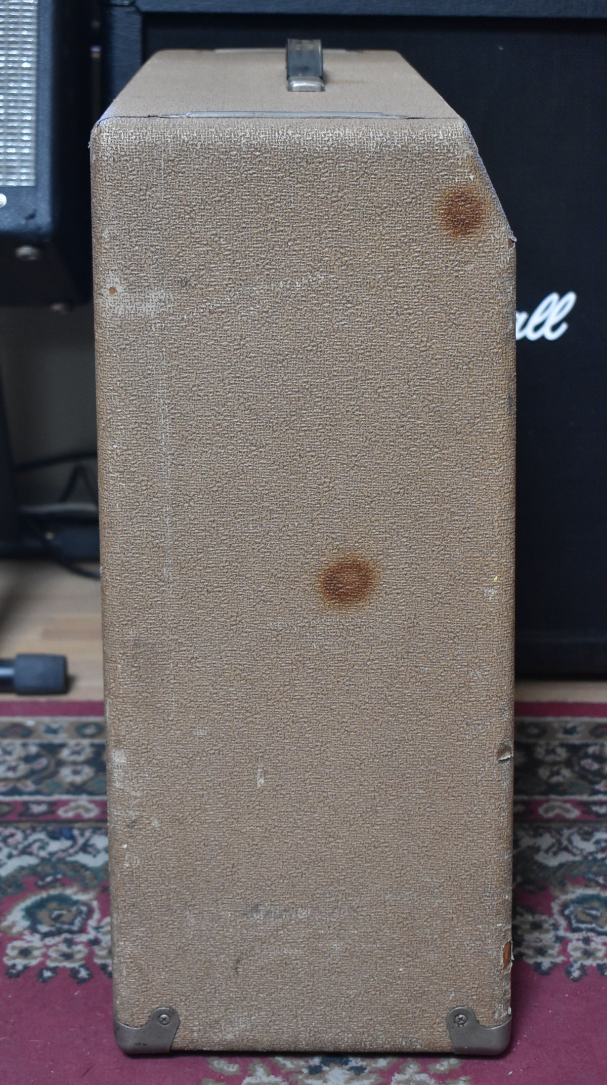 The brown textured amplifier is shown from the right side, revealing a metal handle, two rust spots, and worn metal corner protectors.