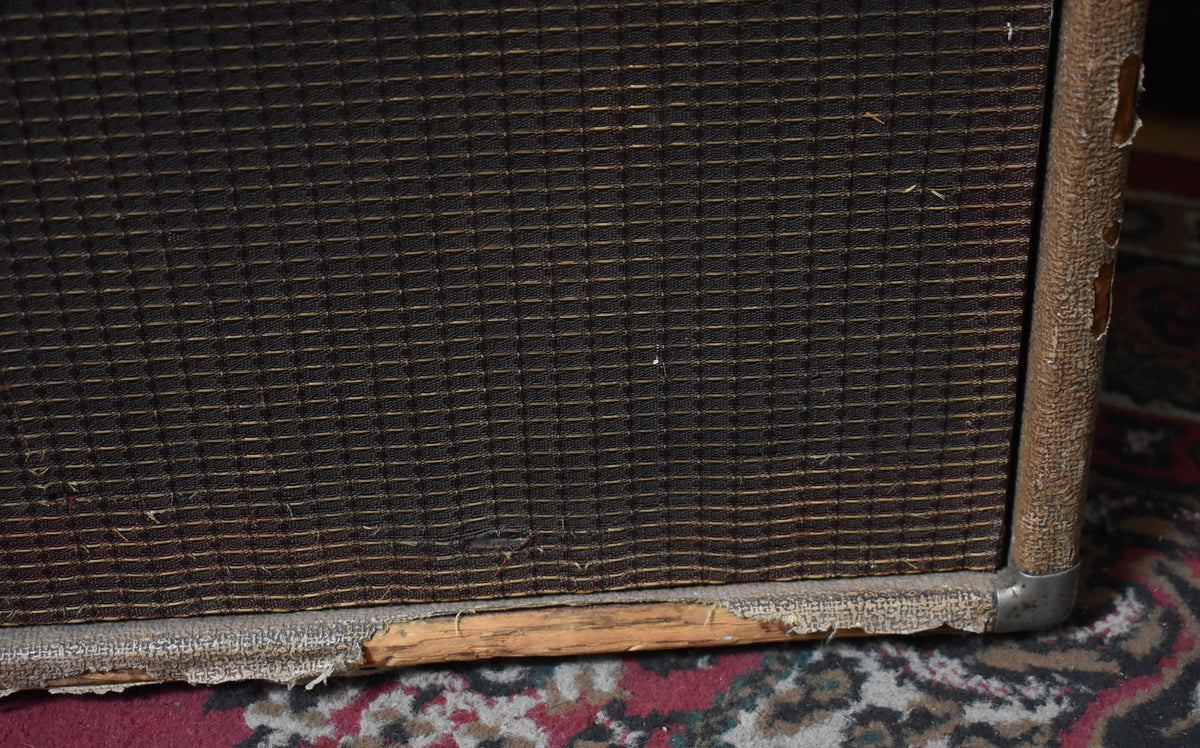 Close-up of the amp's lower right corner, showing the brown grille cloth, worn brown tolex, exposed wood, and metal corner protector.
