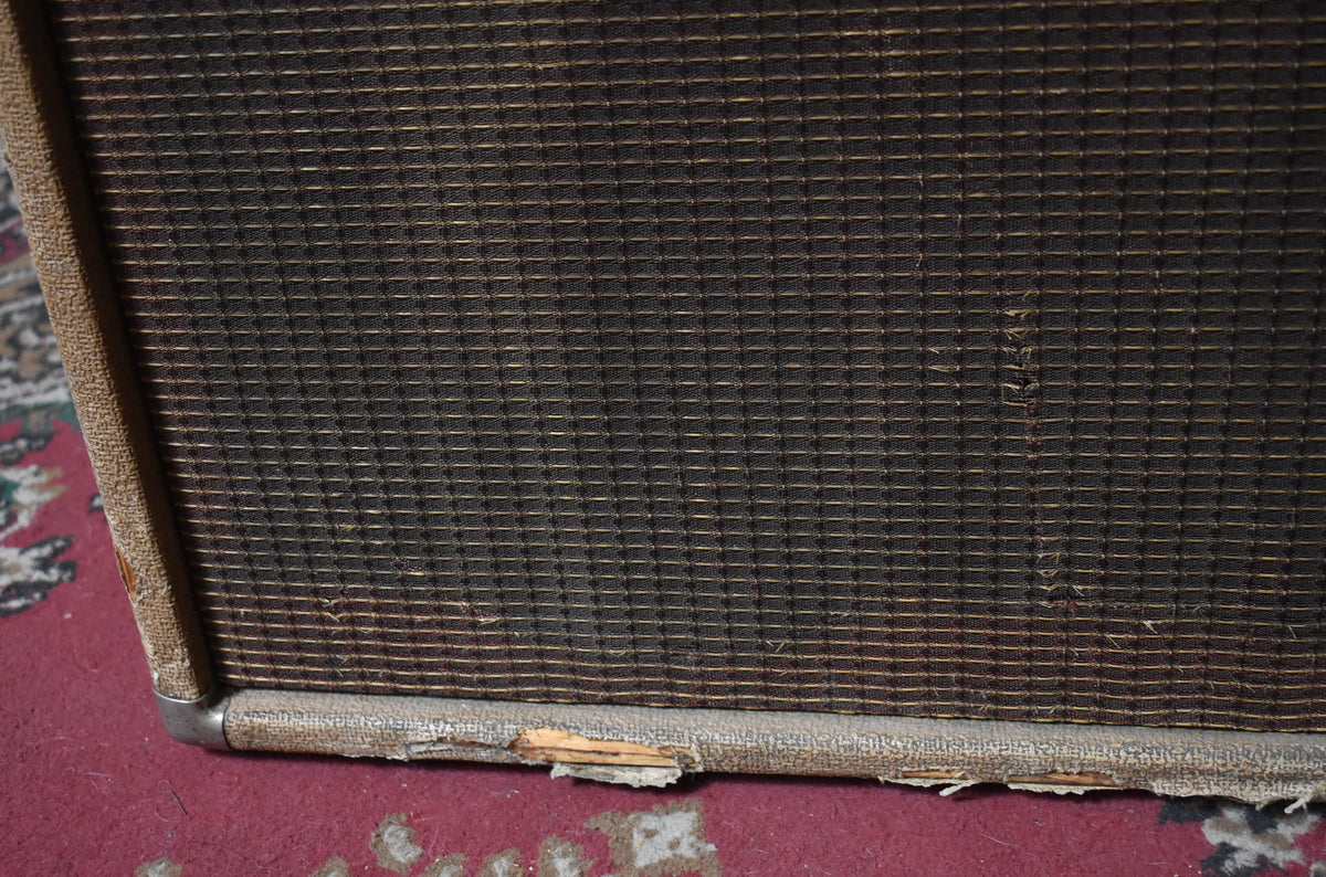 Close-up of the amp's lower right corner, showing a dark brown grille with gold threads, torn tan tolex, and a silver corner protector.