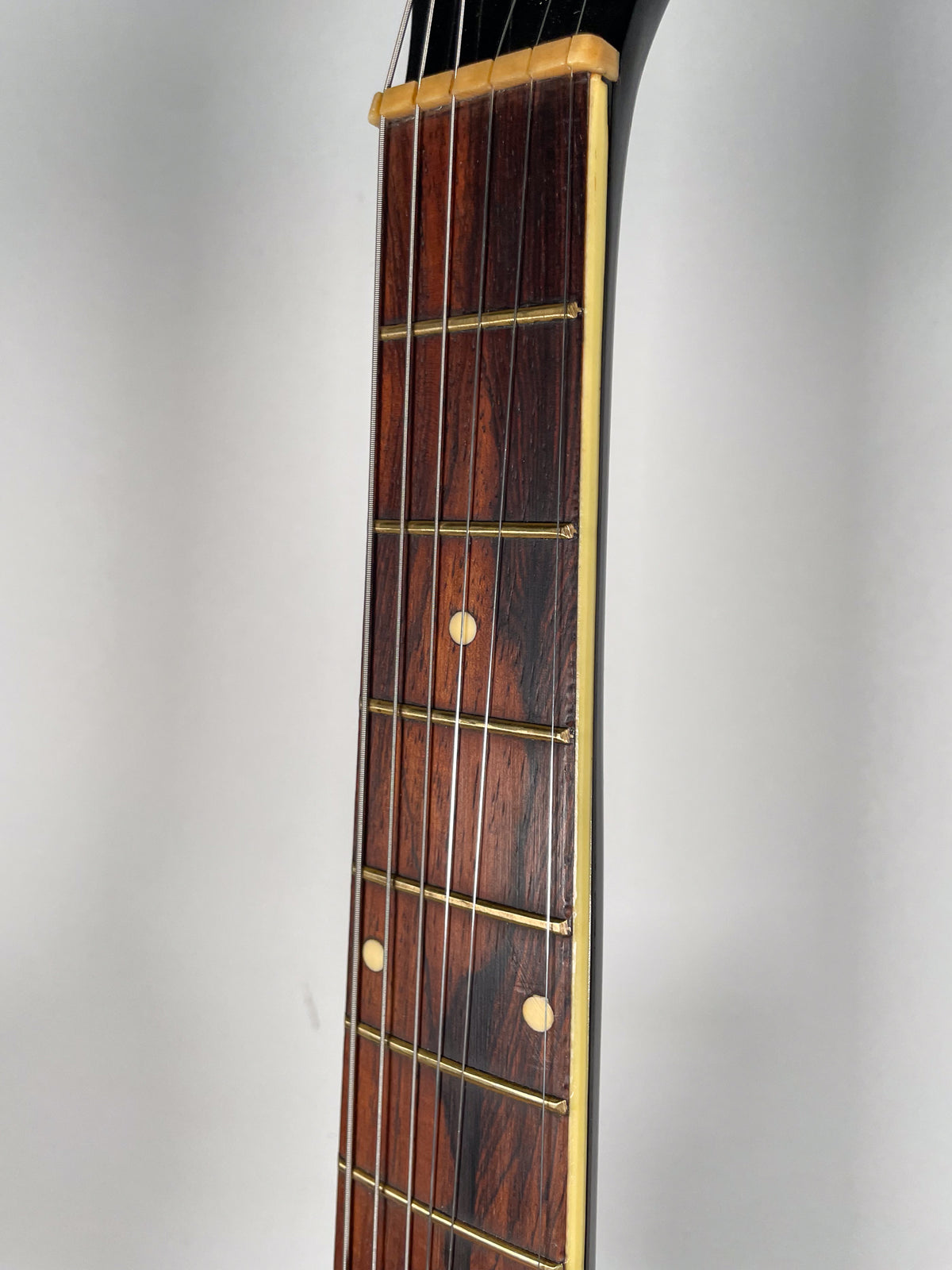 Close-up of the dark rosewood fretboard with light cream binding, showing brass frets and three circular fret markers.