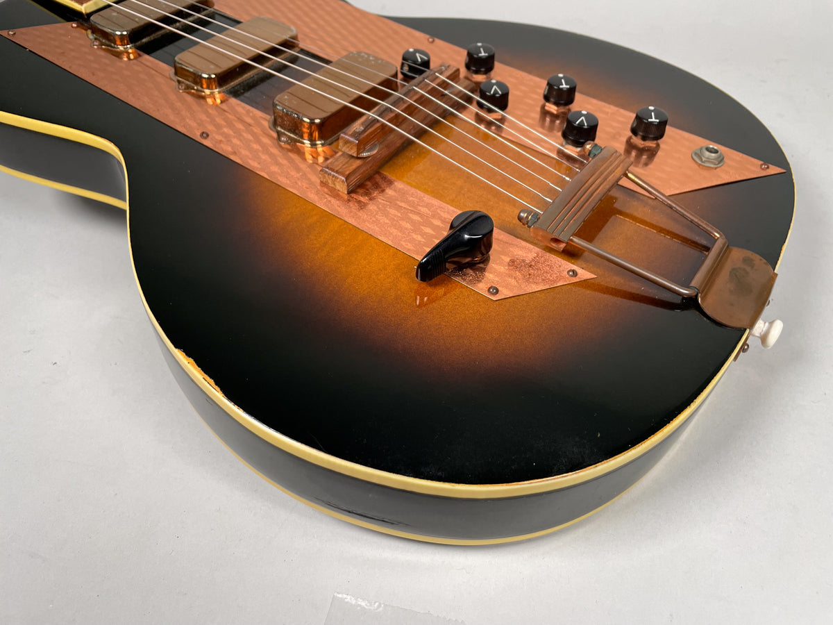 Close-up of the sunburst body, showing the copper pickguard, two pickups, four black knobs, and a trapeze tailpiece.