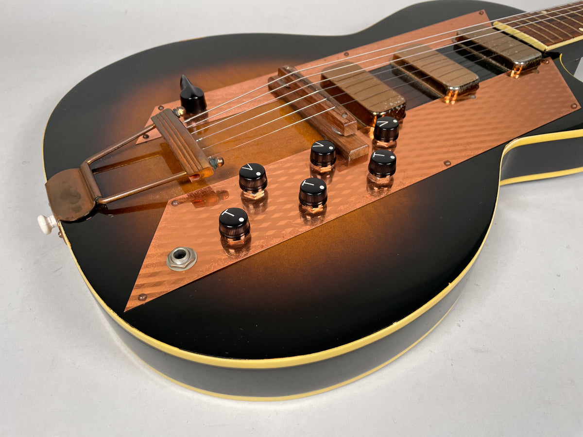 Close-up of the sunburst body, showing the copper pickguard, six black control knobs, two gold pickups, and trapeze tailpiece.