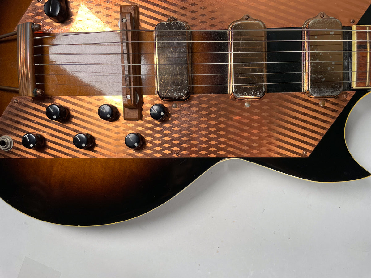 Close-up of the sunburst body, showing the copper-colored pickguard with diagonal stripes, six black control knobs, and three worn pickups.