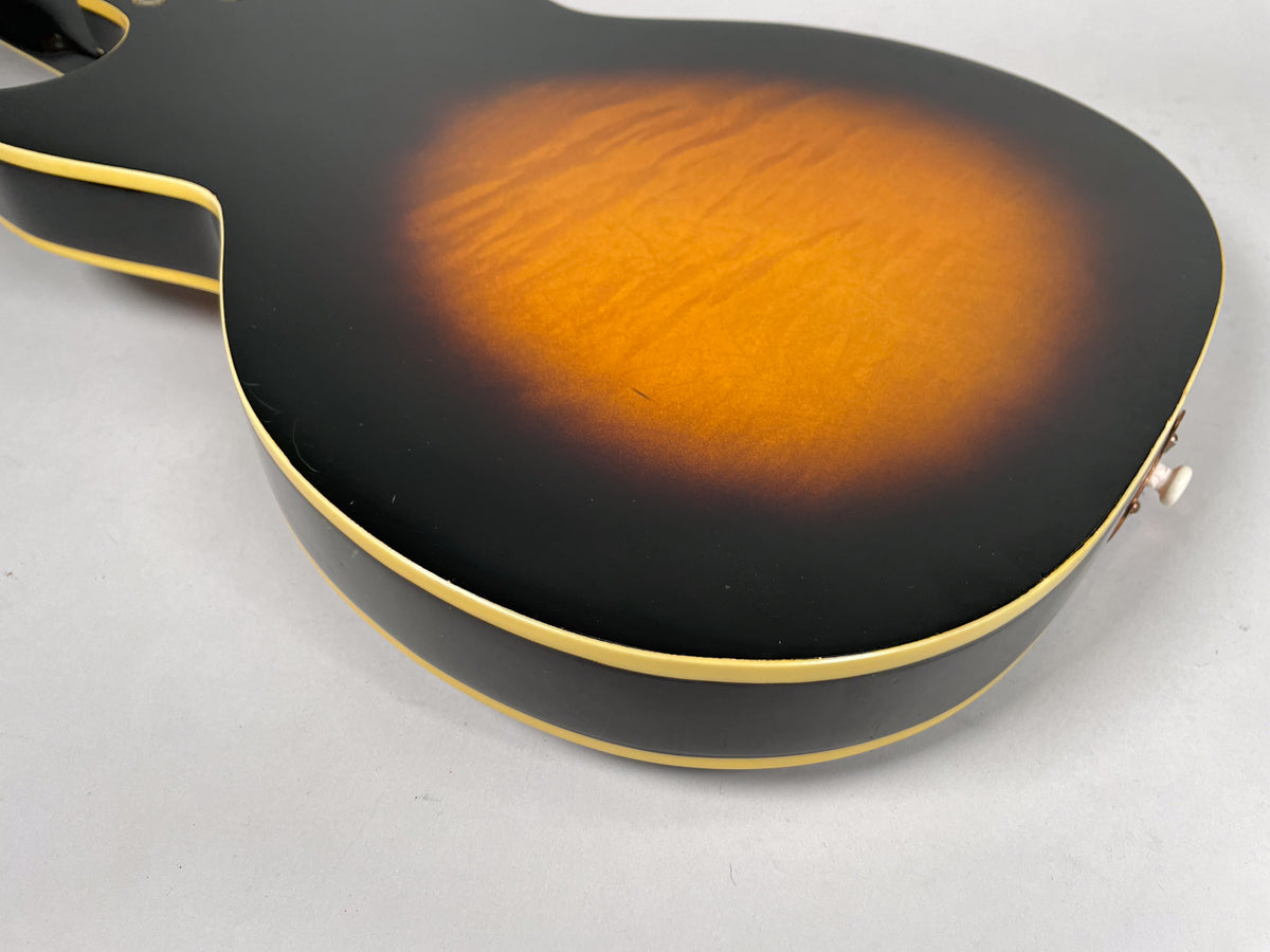 The guitar's sunburst back, showing dark edges fading to orange, with cream binding and a visible output jack.