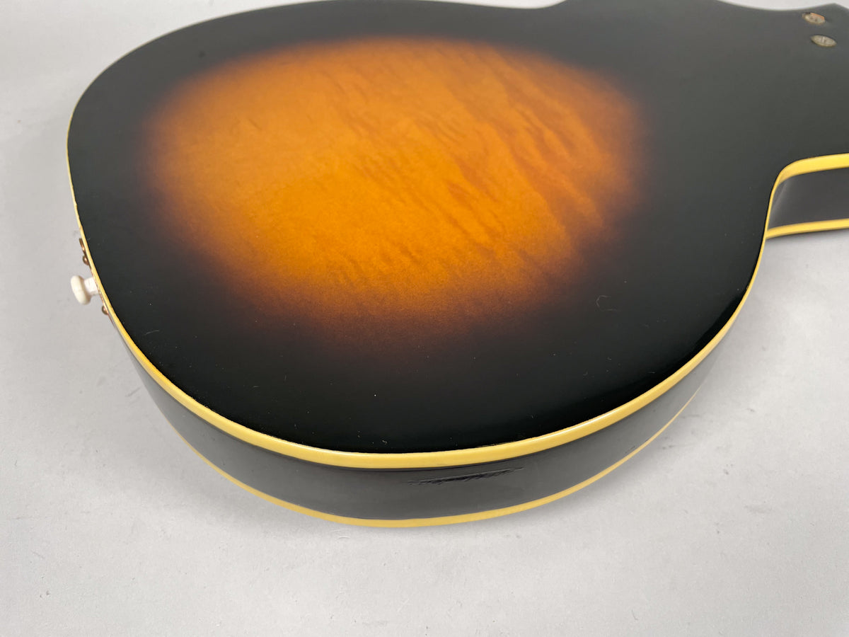The guitar's sunburst back, showing a chip in the black finish near the cream binding on the lower bout, with a strap button visible.