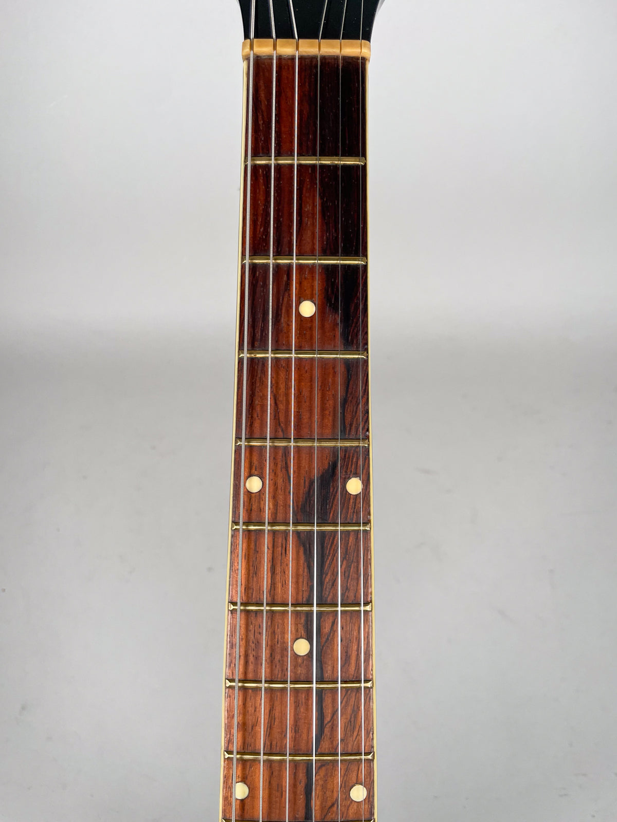 Close-up of the dark brown fretboard with light wood grain, showing six frets with round cream-colored inlays.