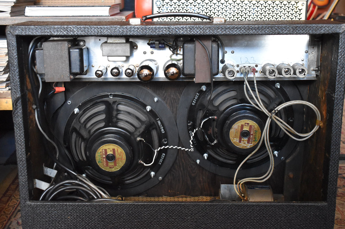 Rear view of the open black combo amp, revealing two large black speakers, several vacuum tubes, and internal wiring.