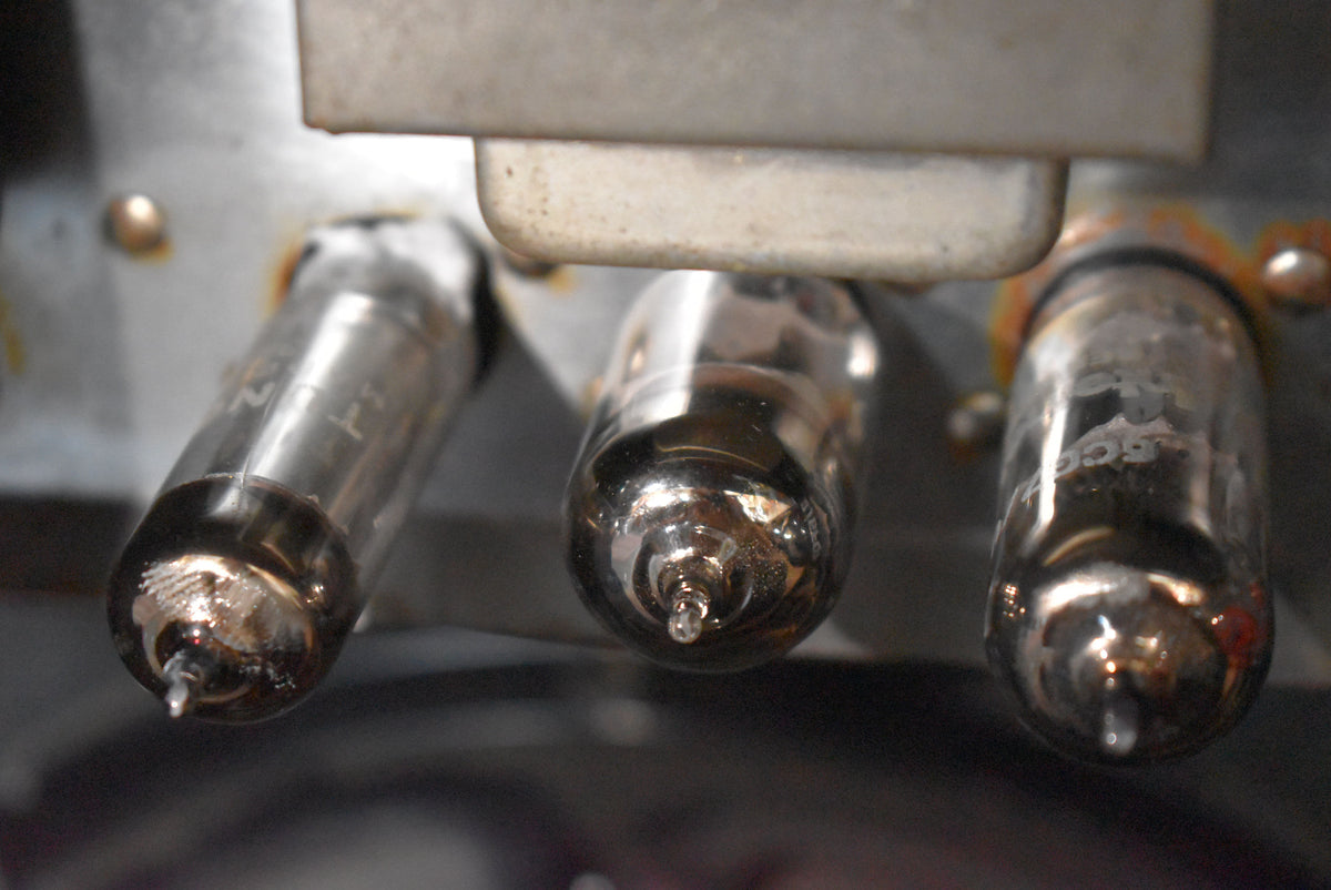 Close-up of three clear glass vacuum tubes with silver bases, showing rust and wear on the metal chassis.