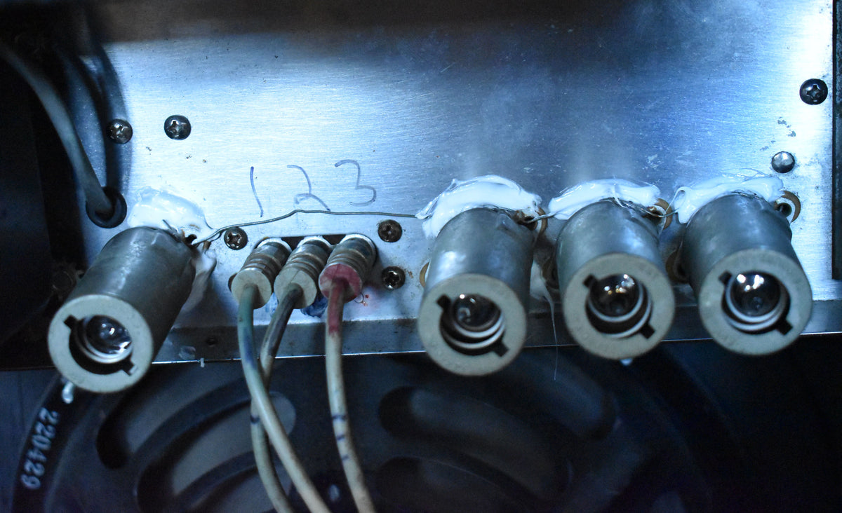 Close-up of the amp's brushed metal chassis, showing four tube sockets with white sealant and three connected cables.