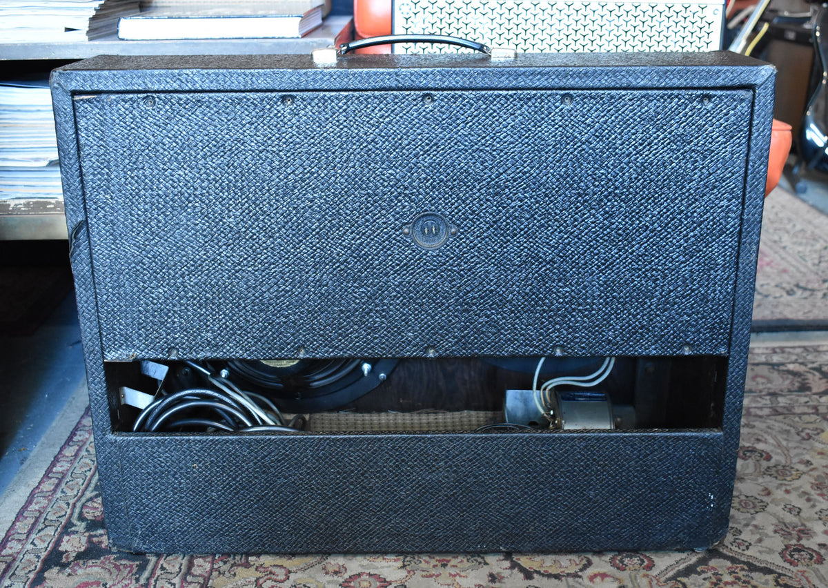 Rear view of a dark gray textured combo amp with a black handle, open back panel revealing internal wiring, and a speaker.