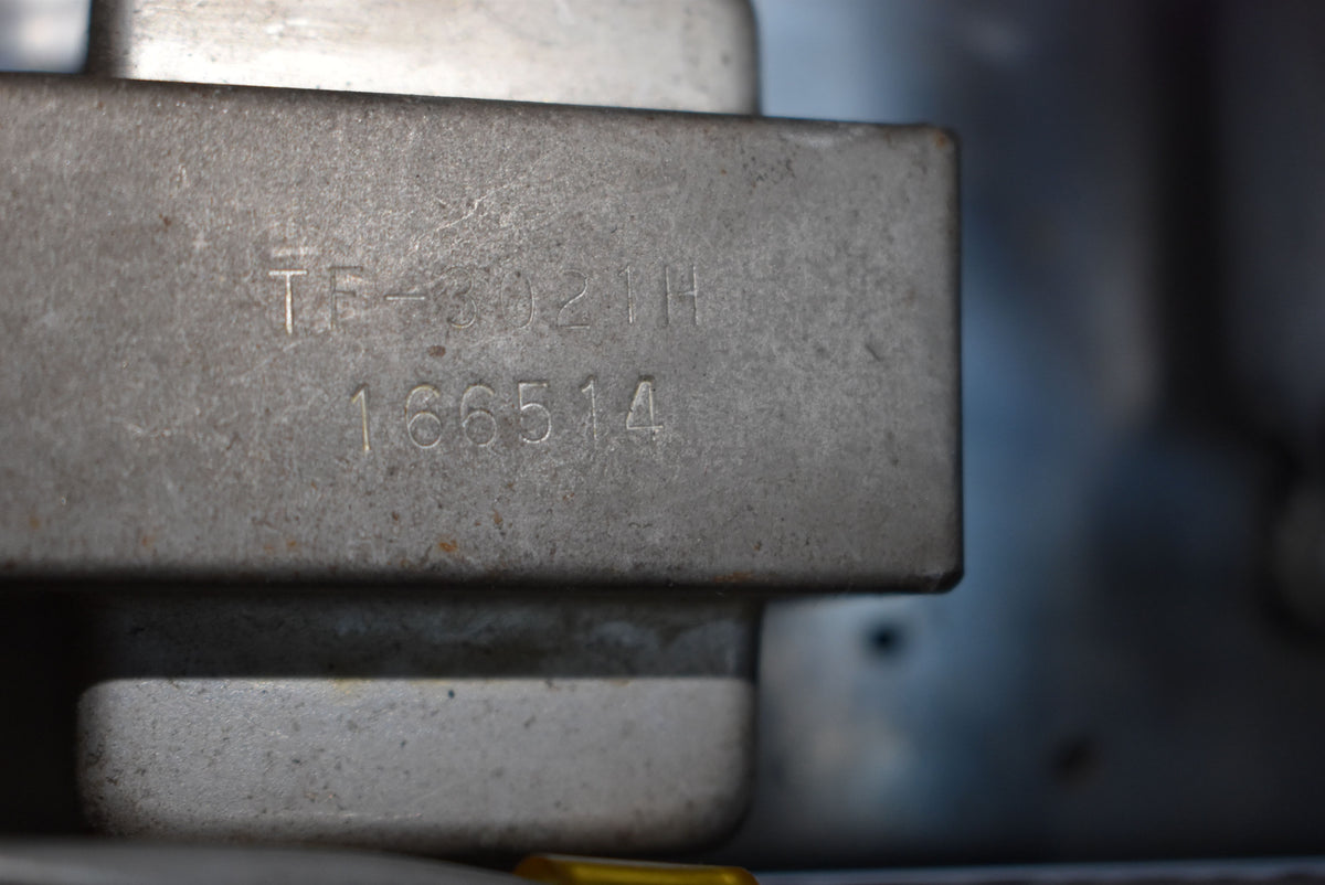 Close-up of a tarnished silver-grey metal component with stamped numbers "TF-3021H" and "166514" on its surface.