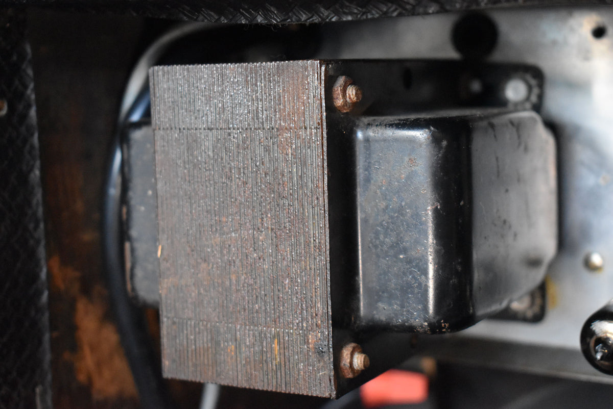 Close-up of the amplifier's internal transformer, showing its black housing and rusted, layered metal core, secured by rusty bolts.