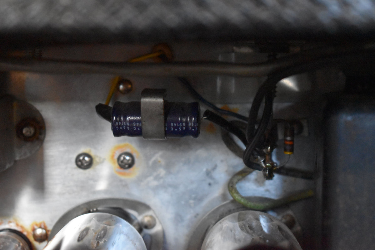 Close-up of the amplifier's internal chassis, showing two dark blue capacitors, wiring, and some rust around mounting screws.