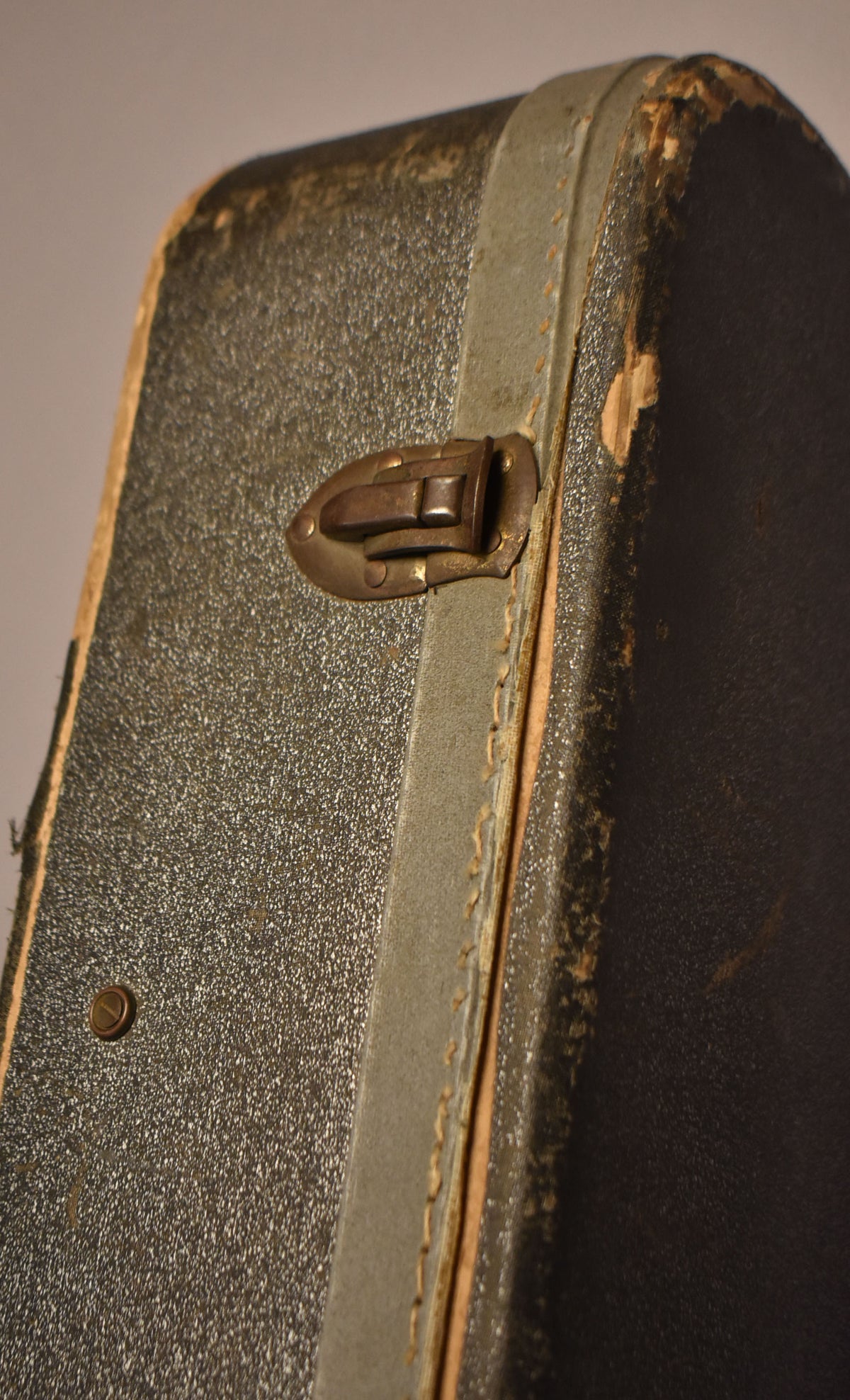 Close-up of a dark grey case with a tarnished brass latch, showing wear on the binding and exposed wood on the top right corner.