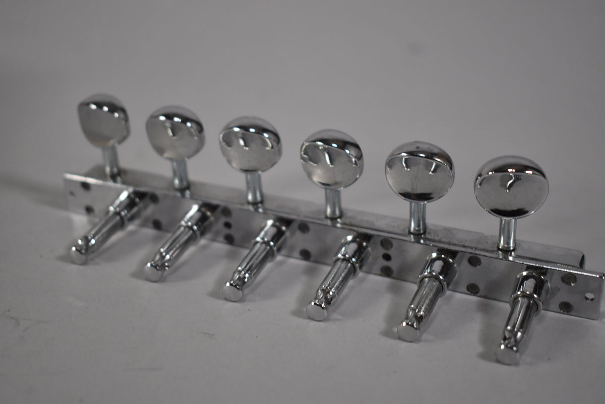 Six chrome tuners with oval buttons are mounted on a metal strip, angled from the lower right to the upper left.