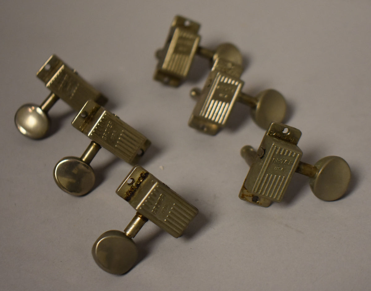 Six tarnished gold-plated tuners with oval buttons are scattered on a gray surface, showing visible wear and oxidation.