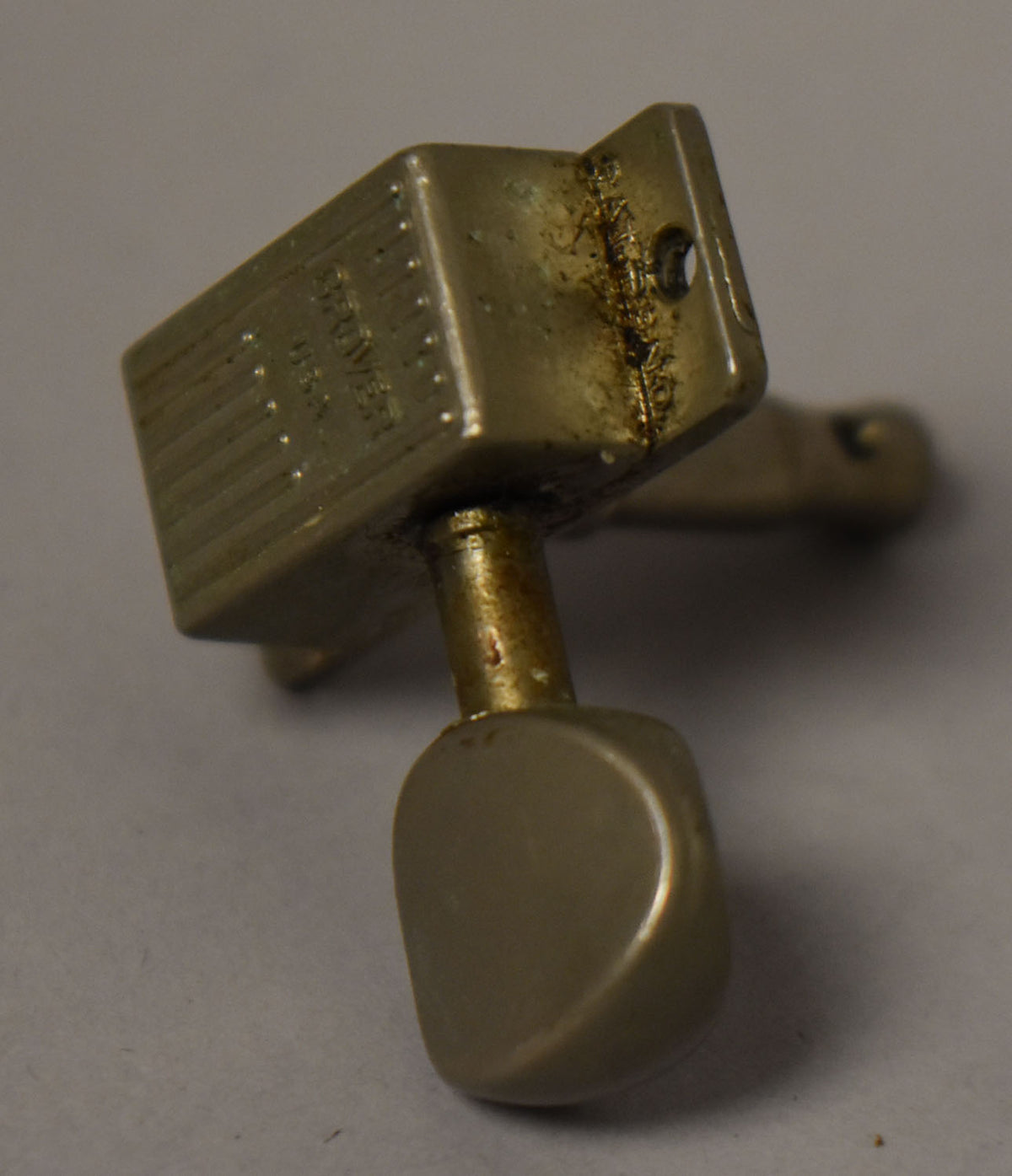 A single, tarnished gold-plated tuner with a rectangular housing and a cream-colored plastic button, viewed from the side.