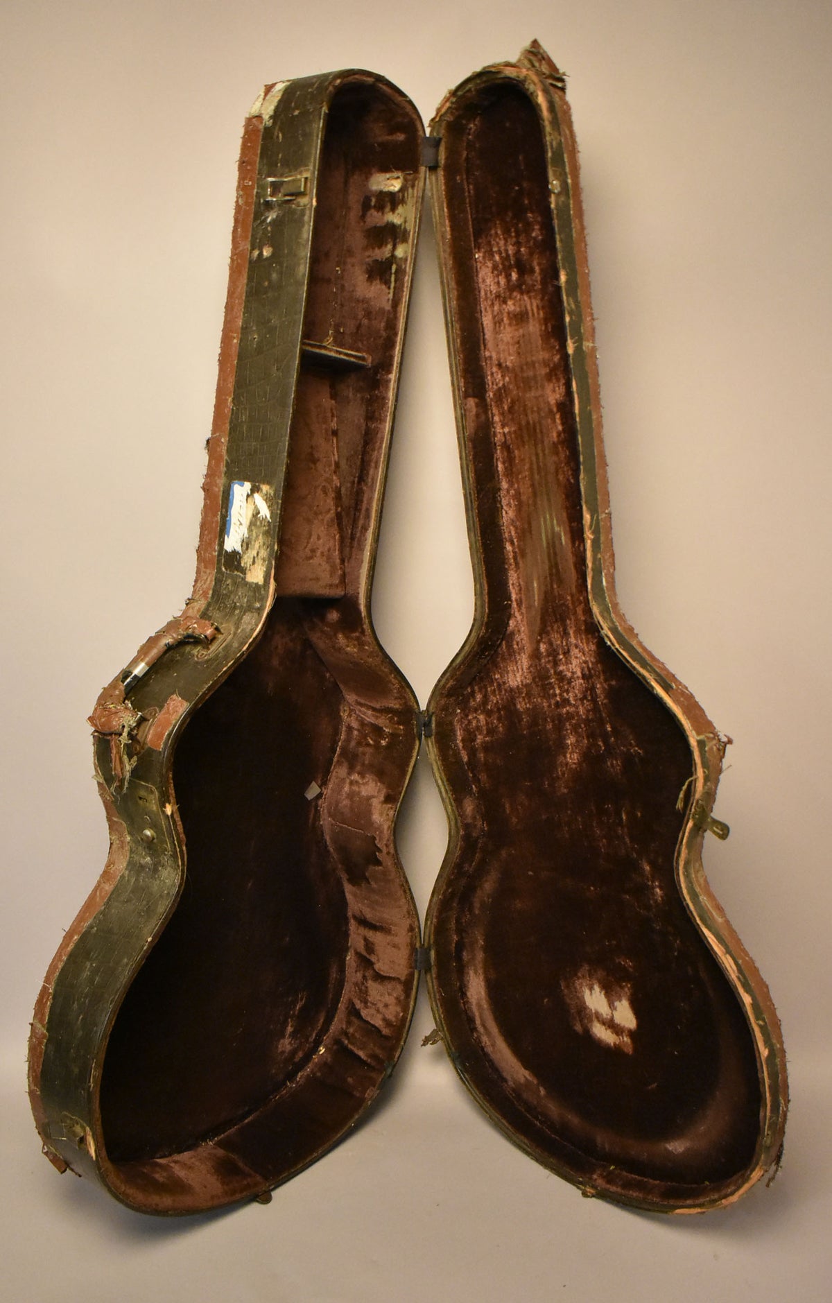 An open, worn faux alligator case with a dark green exterior and tattered brown velvet interior, viewed from above.