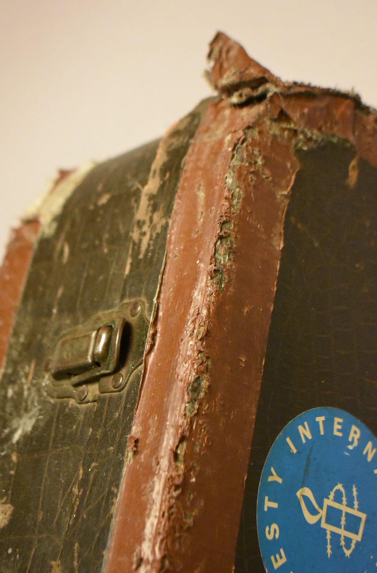 Close-up of the case's dark brown faux alligator finish with a tarnished brass latch, showing significant wear and peeling on the reddish-brown binding.
