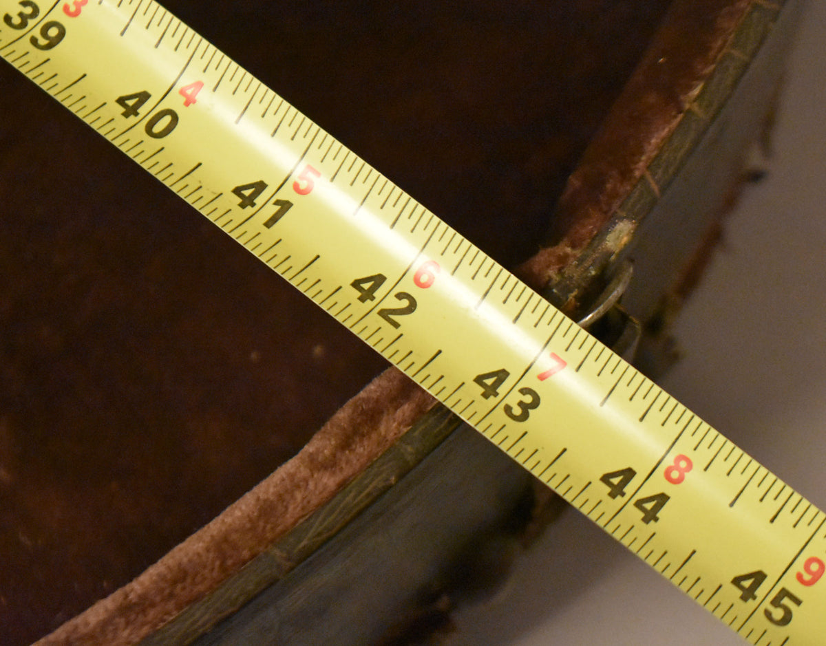 A yellow tape measure diagonally crosses the open case, showing the brown faux alligator exterior and worn brown plush interior.