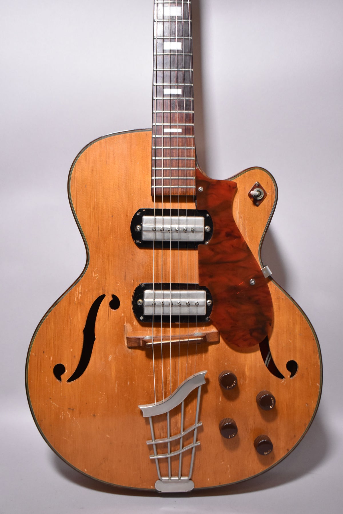 Full-frame view of the natural finish archtop electric guitar, showing two chrome pickups, a tortoiseshell pickguard, and four brown control knobs.