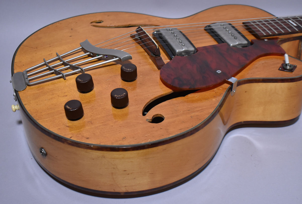 Close-up of the natural finish archtop guitar's lower bout, showing four dark brown knobs, two chrome pickups, and a tortoiseshell pickguard.