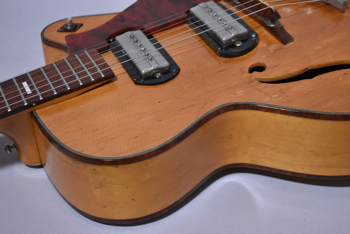 Close-up of the natural finish archtop guitar's body, showing two chrome pickups, a dark red pickguard, and an f-hole.