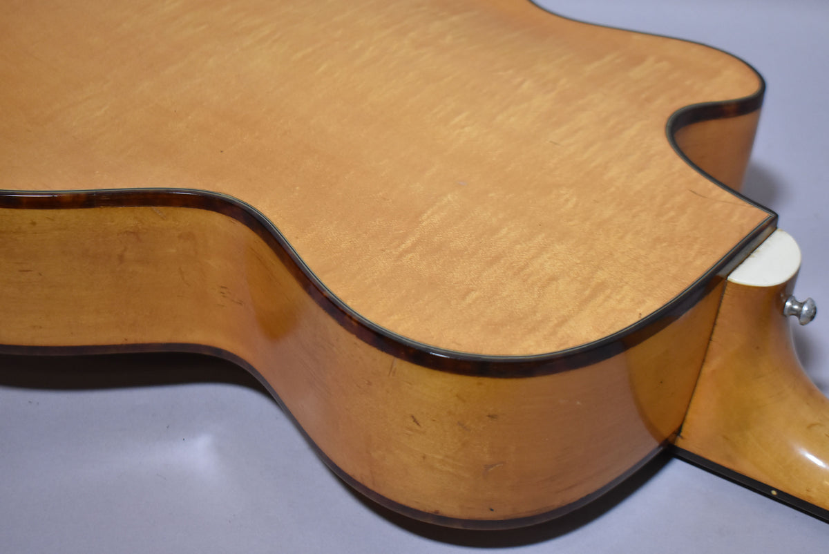 Close-up of the guitar's lower bout and cutaway, showing the natural finish, tortoise binding, and a strap button on the heel.