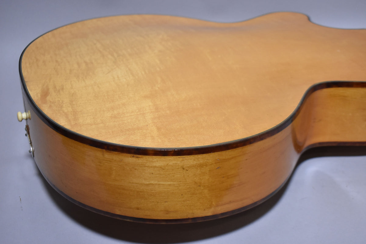 The natural finish archtop guitar's lower bout and cutaway are visible from the back, showing light wear and a cream strap button.