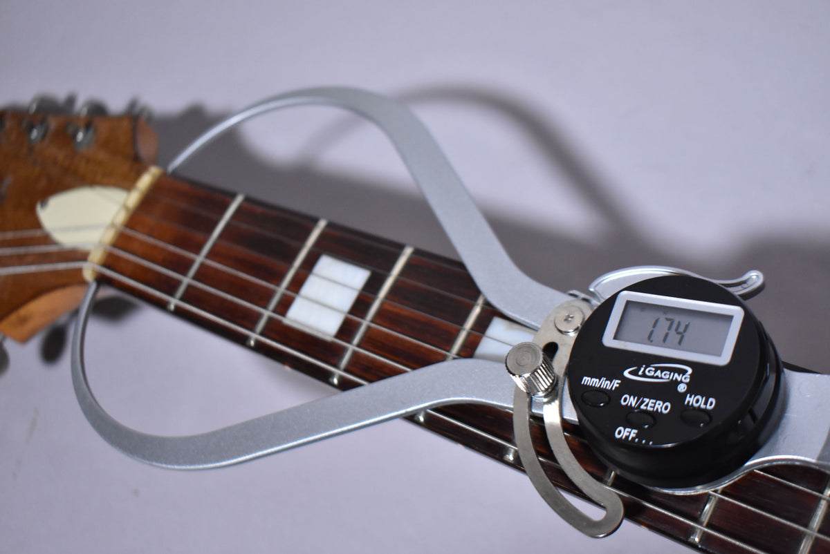 Close-up of the guitar's dark fretboard with rectangular white inlays, showing a digital caliper measuring the nut width at 1.74 inches.