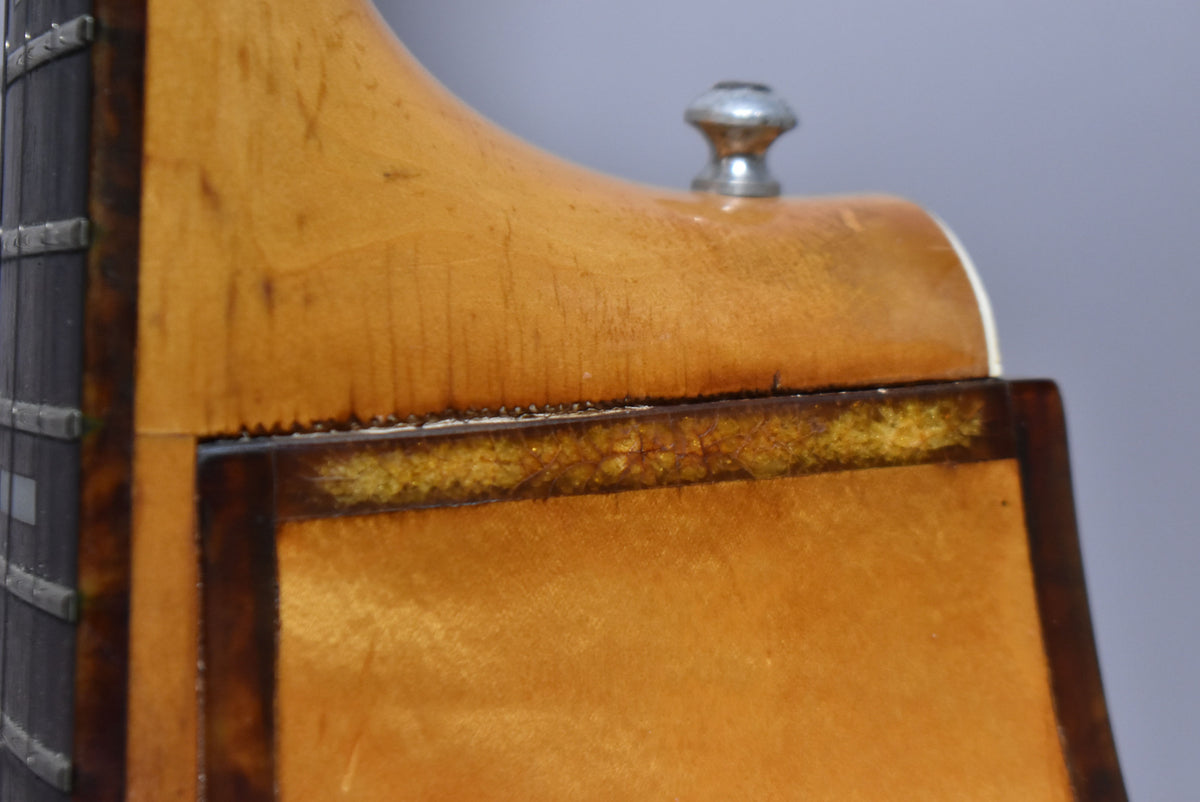 Close-up of the natural finish guitar's neck heel and body, showing finish checking and a strap button.