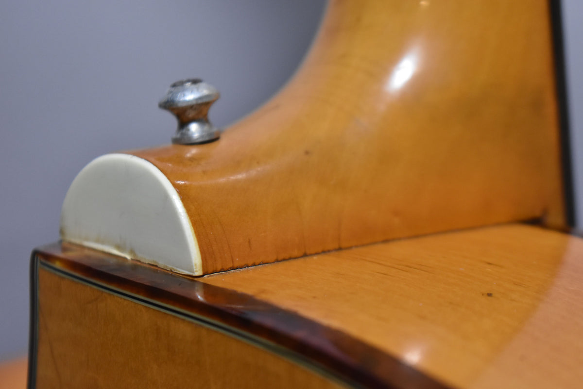 Close-up of the guitar's natural finish neck heel and body, showing a white cap, a strap button, and finish checking along the joint.