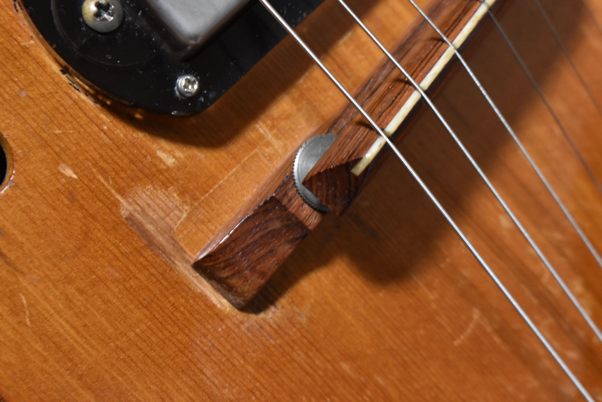 Close-up of the guitar's natural finish body, showing a dark wood bridge with metal adjusters, a black pickup, and visible wear.