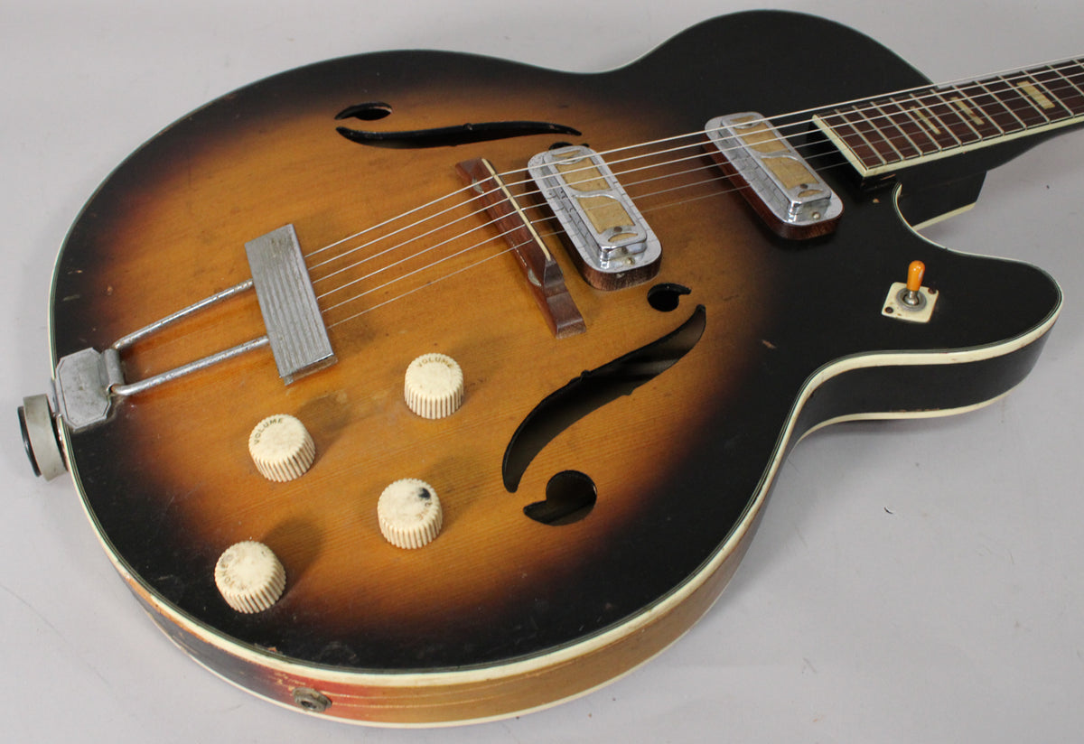 The sunburst hollow body guitar, viewed from above, shows two pickups, four cream knobs, a three-way switch, and f-holes.