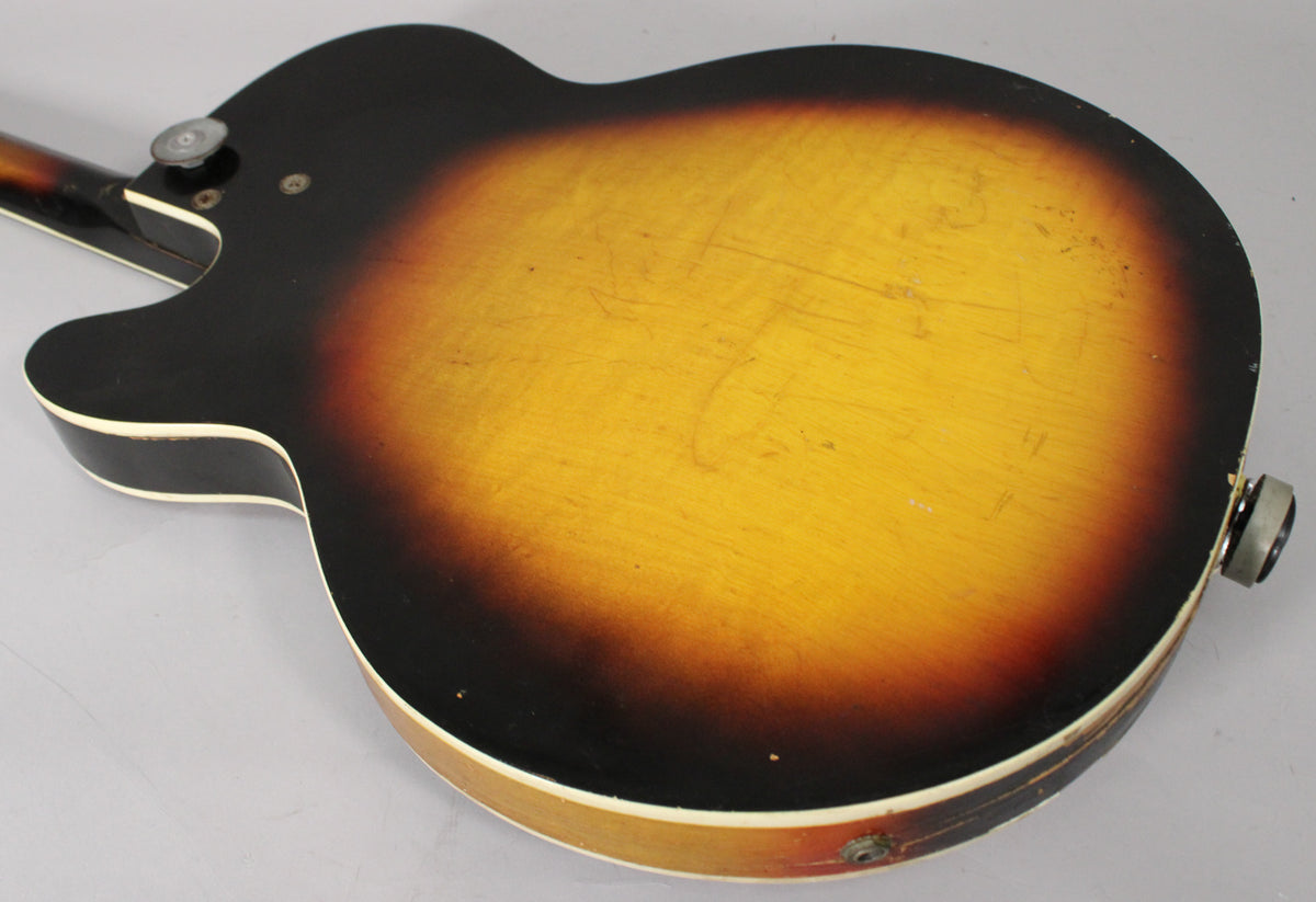 The guitar's back shows a sunburst finish with heavy wear, scratches, and checking, plus a visible output jack and strap button.
