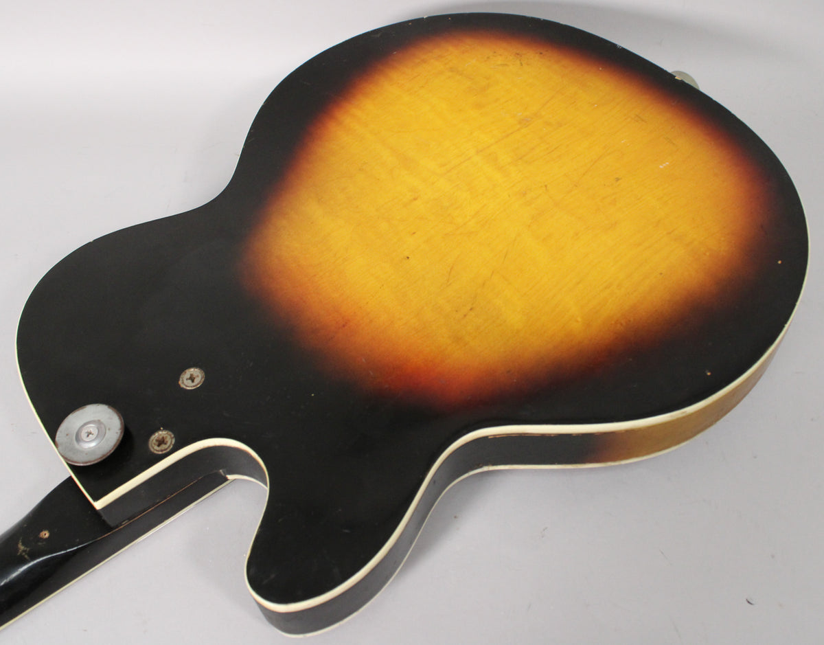 The guitar's back shows a sunburst finish with heavy wear, checking, and scratches, plus a strap button and two screws near the neck joint.