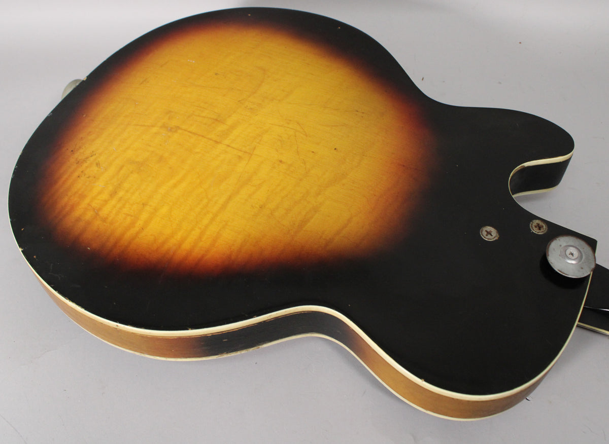The guitar's sunburst back shows heavy finish wear and scratches, with a visible strap button and two screws near the cutaway.