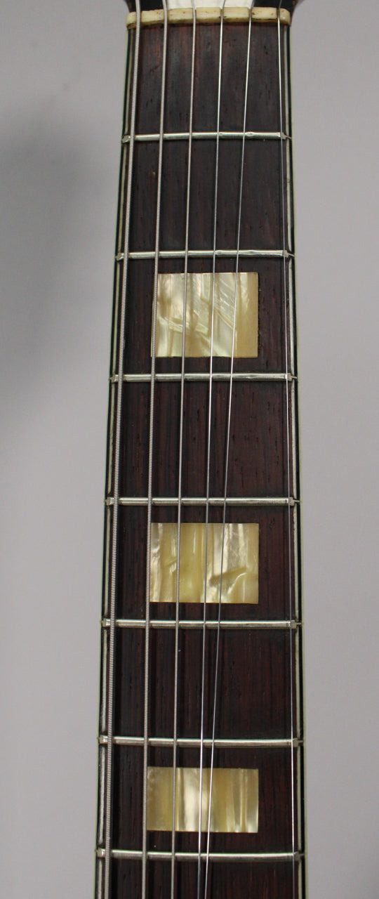 Close-up of the dark brown fretboard with three rectangular mother-of-pearl inlays and visible wear on the frets and strings.