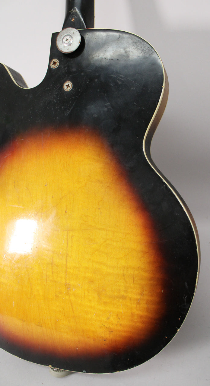 The guitar's sunburst back shows heavy finish checking, scratches, and wear, with a metal strap button near the neck joint.