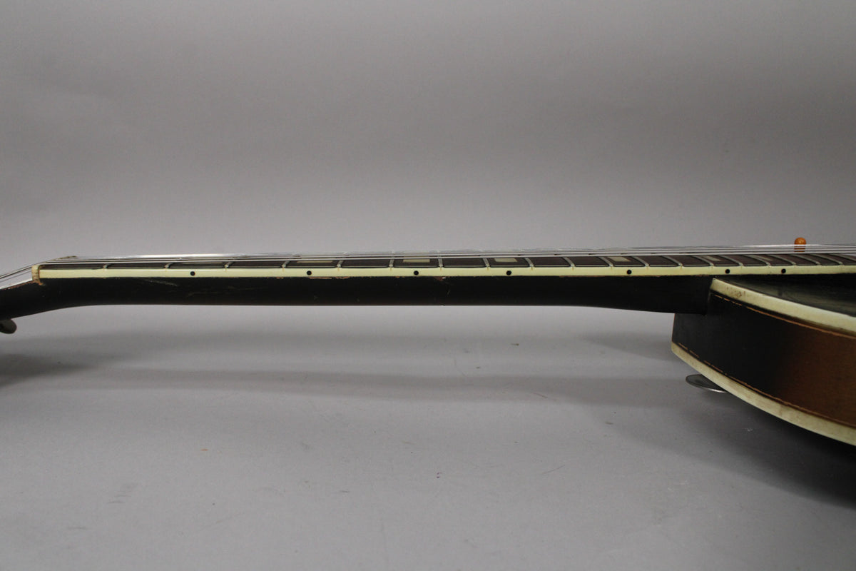 The guitar neck is viewed from the side, showing the dark fretboard with white binding and dot inlays, and some finish wear.