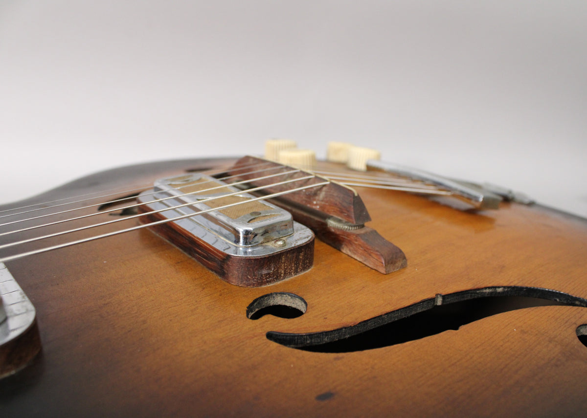 Close-up of the sunburst body, showing the chrome pickup, wooden bridge, f-hole, and two cream control knobs with visible wear.