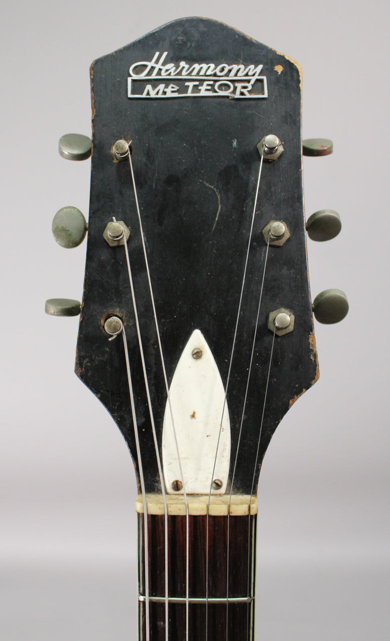 The guitar's black headstock, with six tarnished tuners and a white truss rod cover, shows significant finish wear and chips.