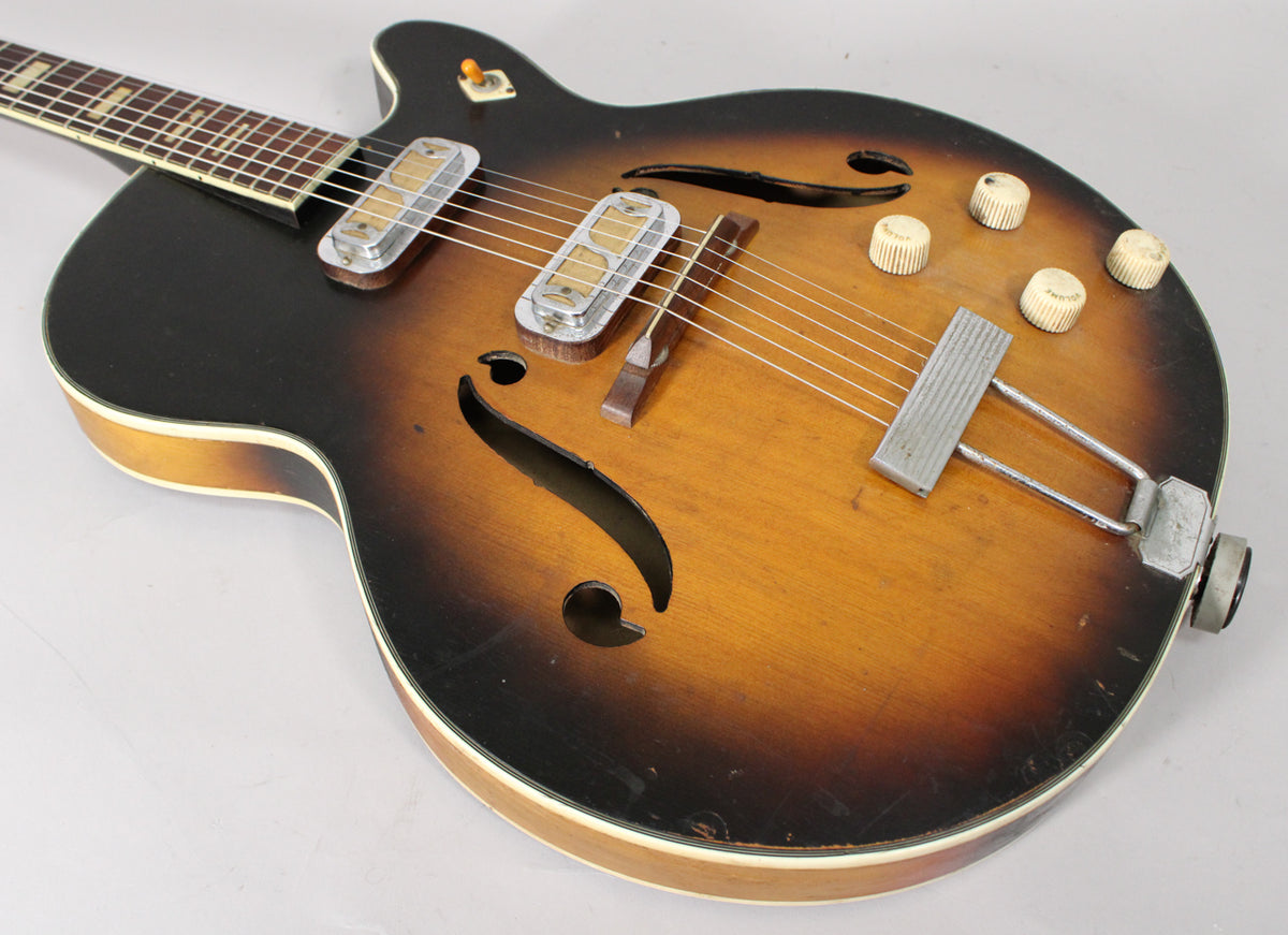 Close-up of the sunburst hollow body, showing two pickups, a trapeze tailpiece, four cream knobs, and f-holes.