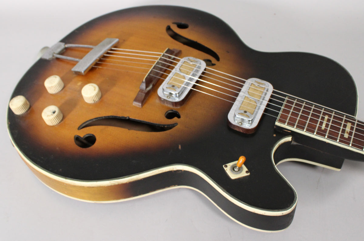 Upper body of a sunburst hollow body guitar, showing four cream knobs, two chrome pickups, and a toggle switch.