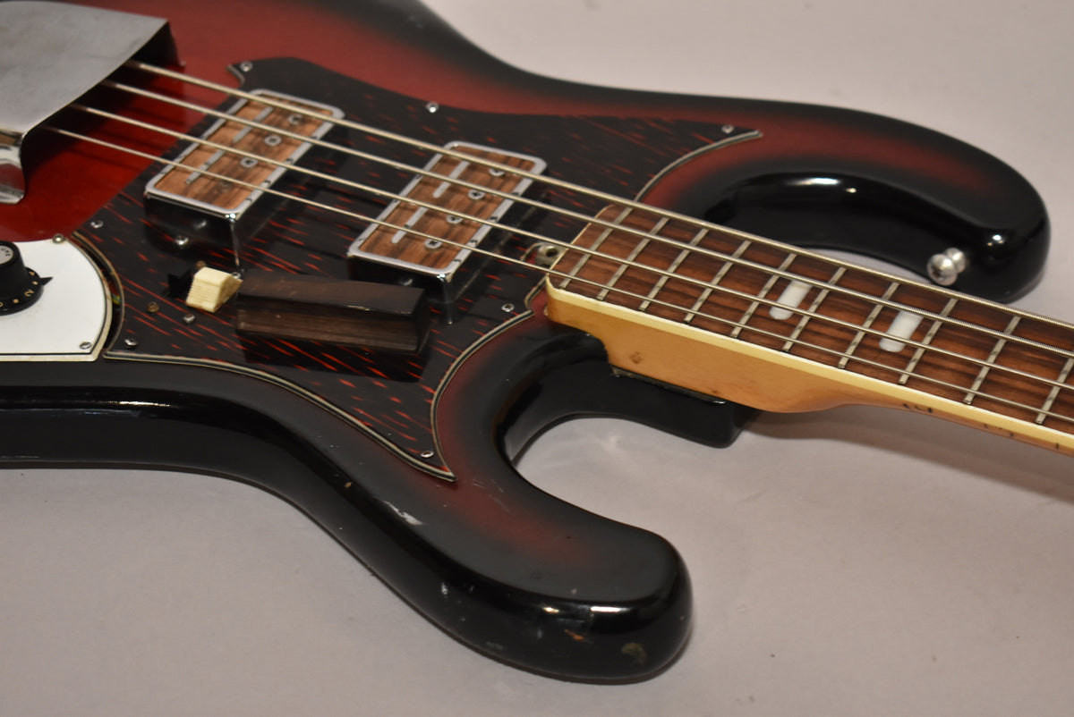 The red burst bass guitar's body and neck are angled, showing the dark tortoiseshell pickguard, two pickups, and a chrome bridge cover.