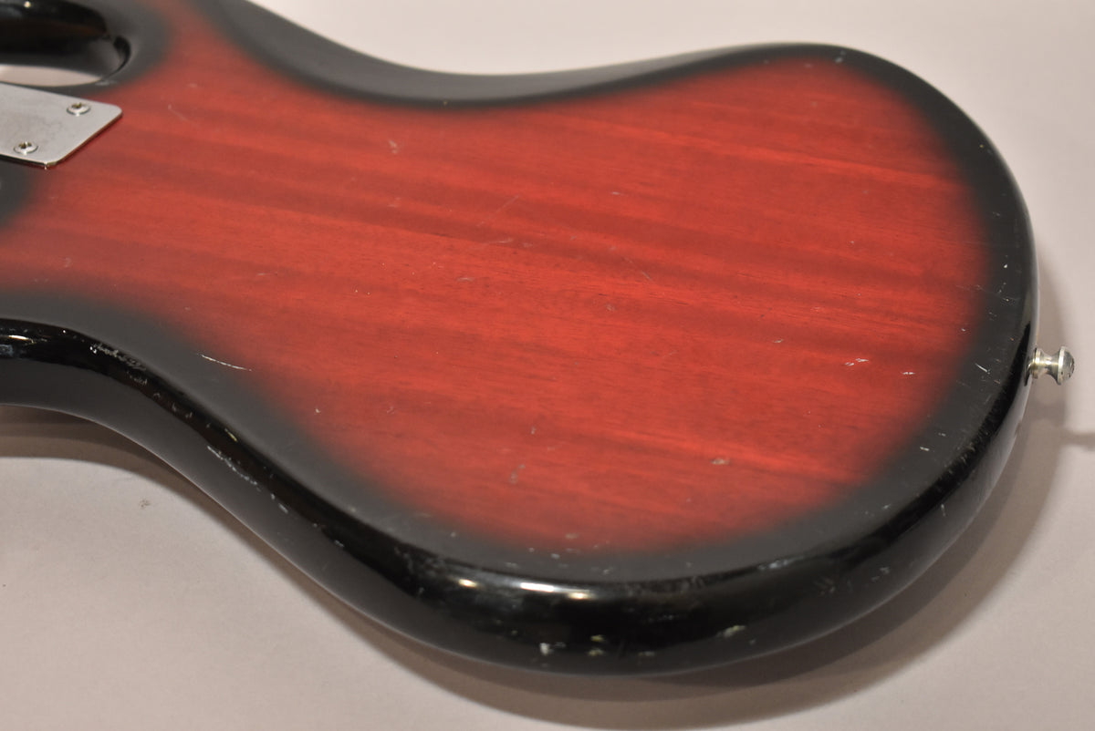 The lower bout of a red burst bass, showing a chrome strap button, body wear, and finish chips along the black edge.