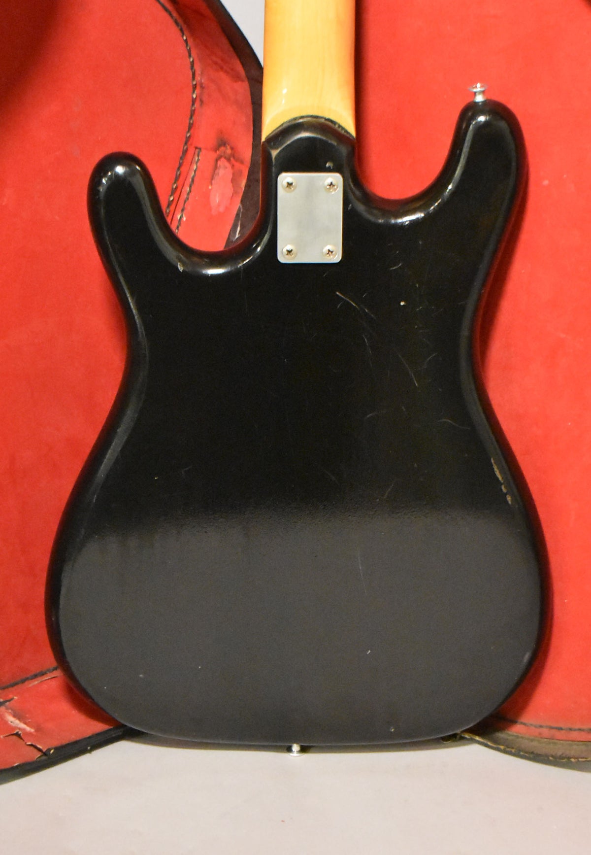 The black solidbody guitar's back is shown, revealing a four-screw neck plate, a strap button, and many surface scratches and dings.