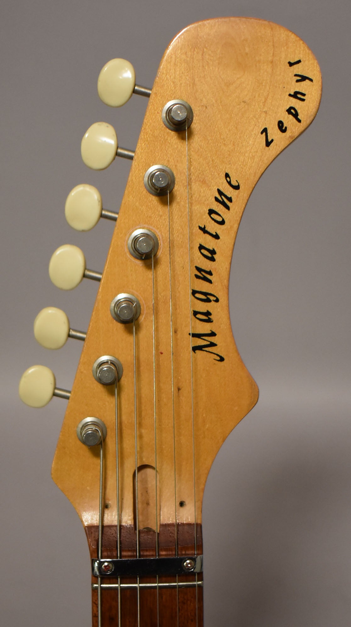 Close-up of the light-colored headstock with six cream tuners, showing some wear and a dark brown fretboard.